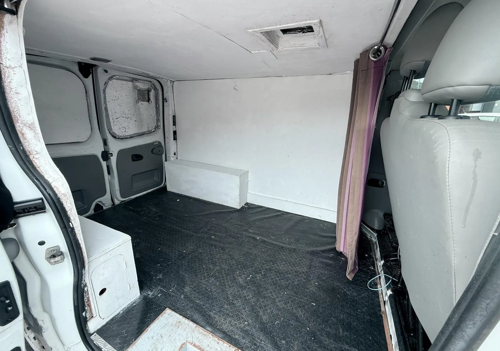 Vue intérieure arrière du fourgon blanc Nissan Primastar 2005 montrant l'espace de chargement vide avec sol noir et sièges gris.