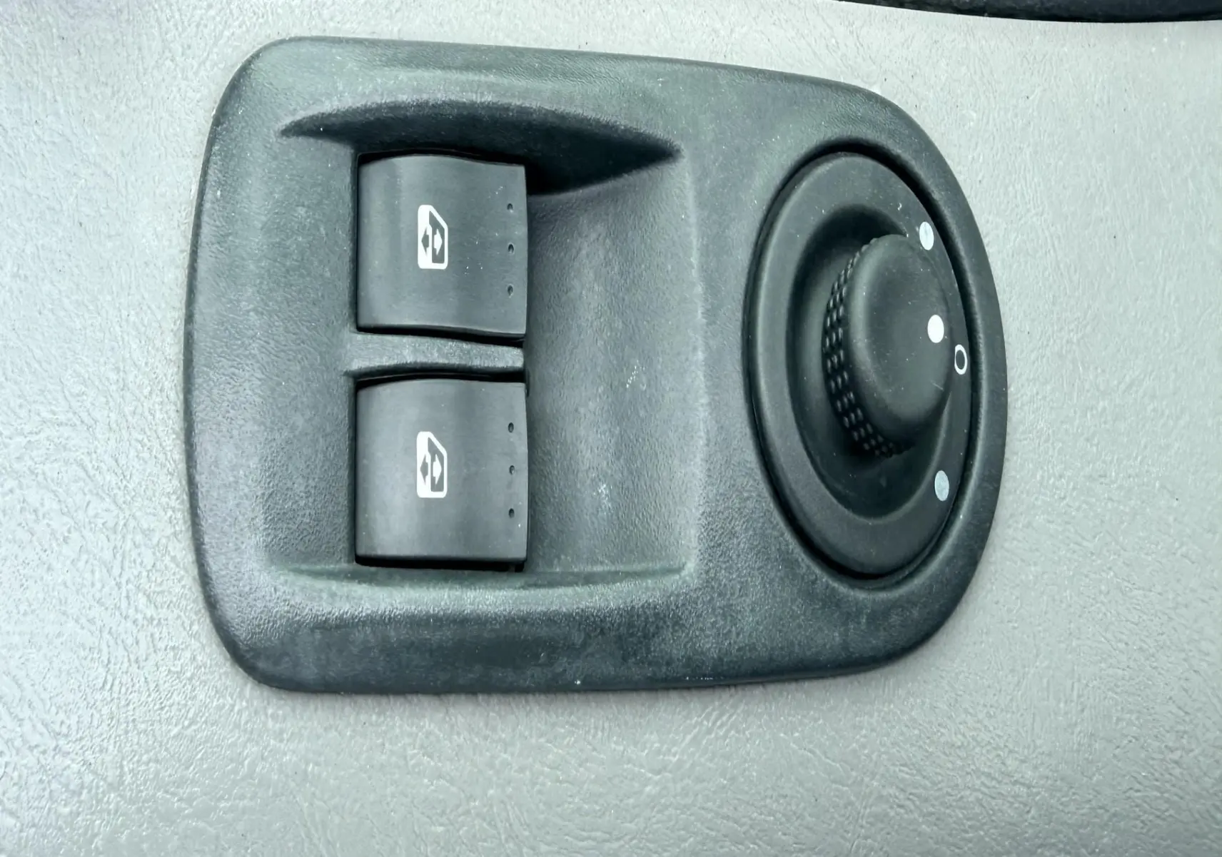 Vue rapprochée des commandes électriques des vitres et du réglage des rétroviseurs sur la portière côté conducteur d’un Nissan Primastar blanc.