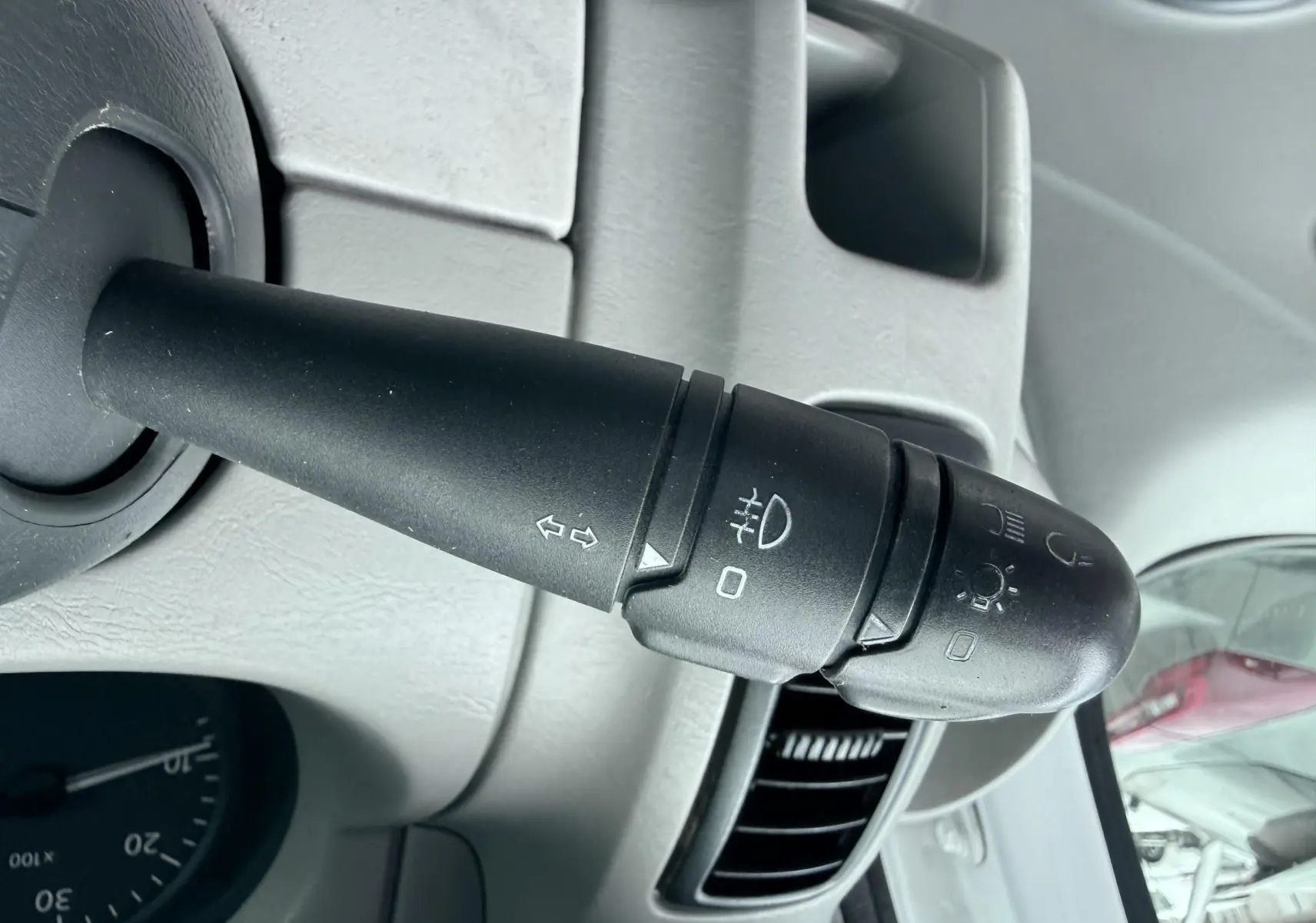 Gros plan sur la manette de clignotants noire à gauche du volant dans l’habitacle gris clair du Nissan Primastar blanc.