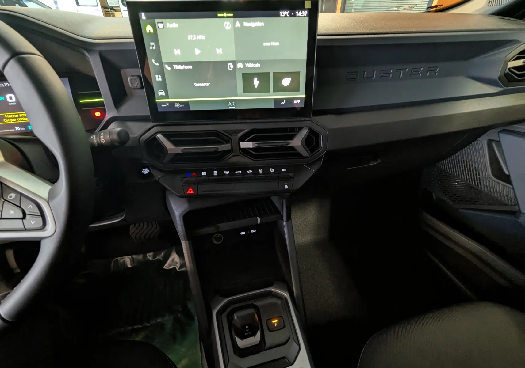 Vue intérieure centrée sur la console et l'écran tactile du Dacia Duster Hybrid 140 blanc glacier, avec levier de vitesse automatique.