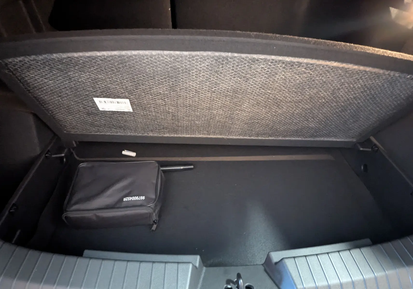 Vue intérieure du coffre ouvert du Dacia Duster Hybrid 140 Journey 2025, montrant un rangement noir avec trousse.