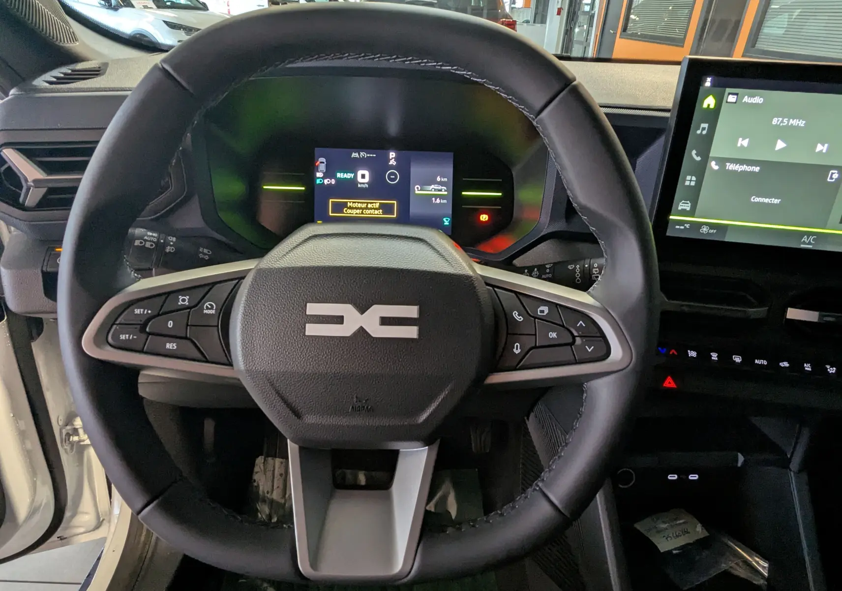 Vue intérieure centrée sur le volant noir du Dacia Duster Hybrid 140 Journey avec tableau de bord numérique et écran tactile.