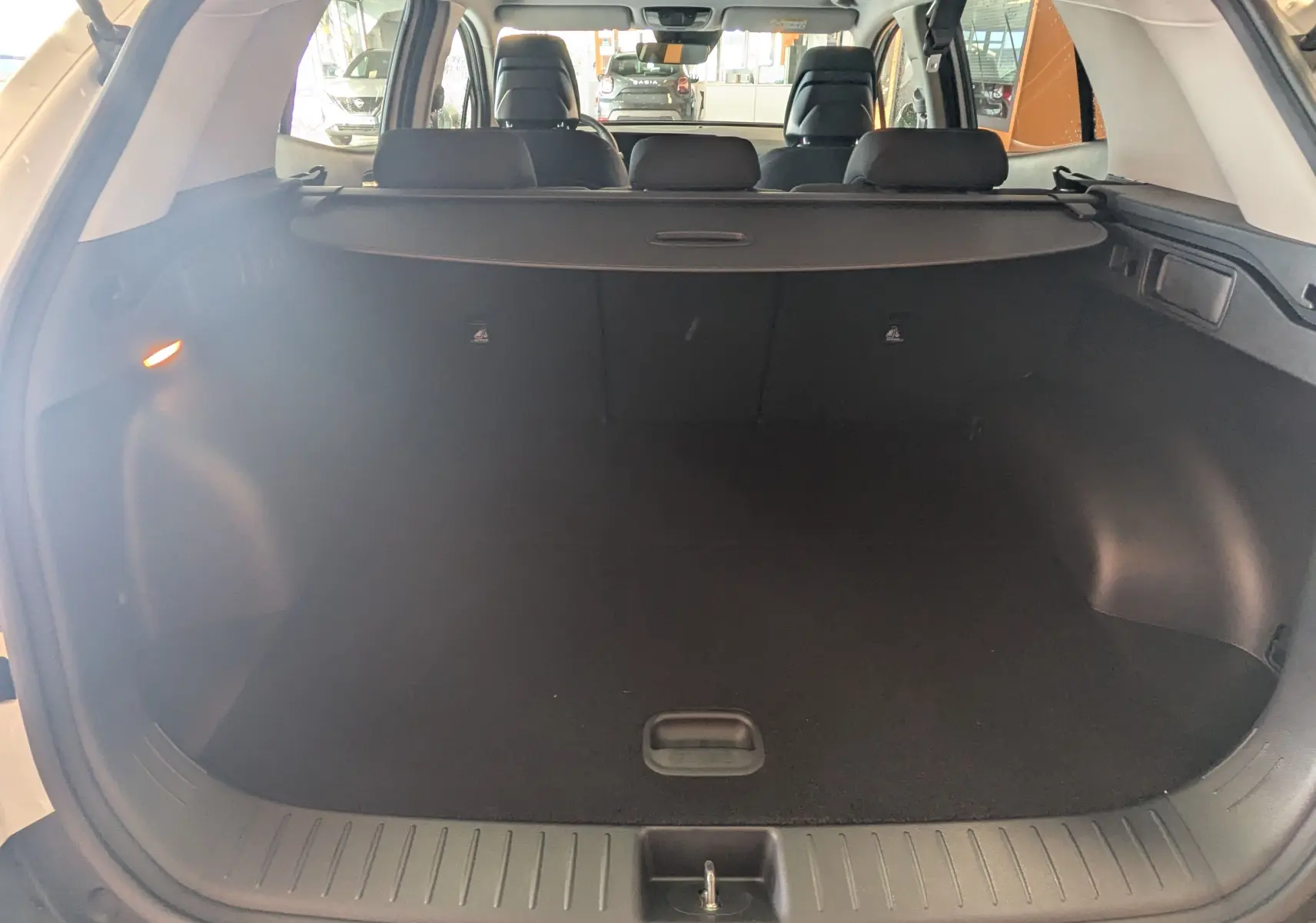 Coffre ouvert vu de l'arrière d'un KIA Sportage blanc 2025, montrant l'espace de chargement et la plage arrière.