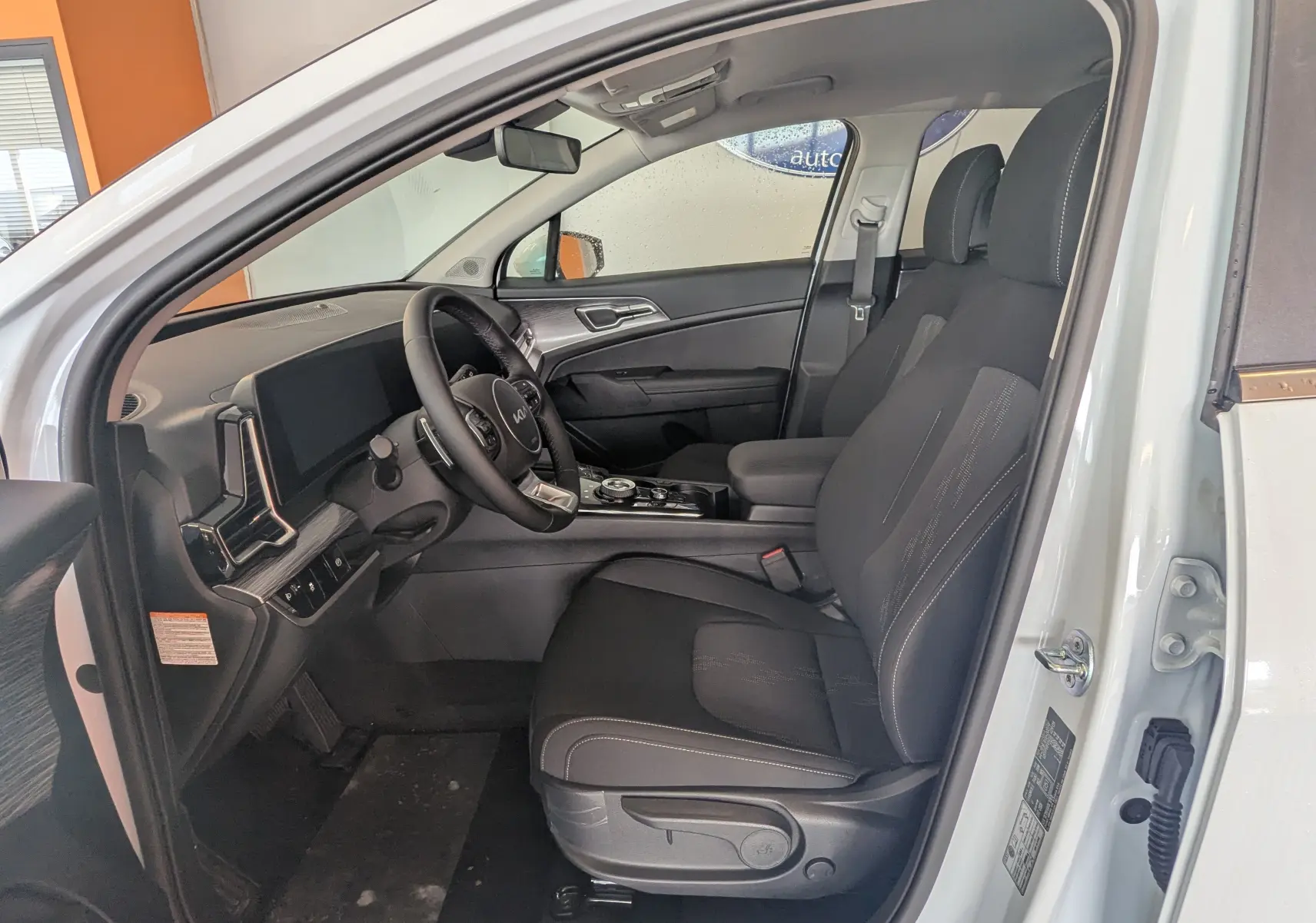 Vue intérieure côté conducteur du Kia Sportage blanc 2025, montrant les sièges noirs et le tableau de bord moderne.