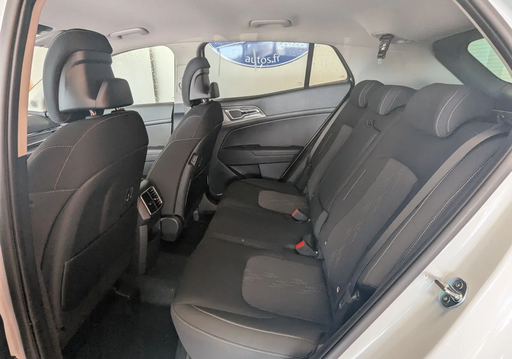 Vue intérieure côté droit des sièges arrière noirs du Kia Sportage blanc 2025, avec appuie-têtes et ceintures visibles.