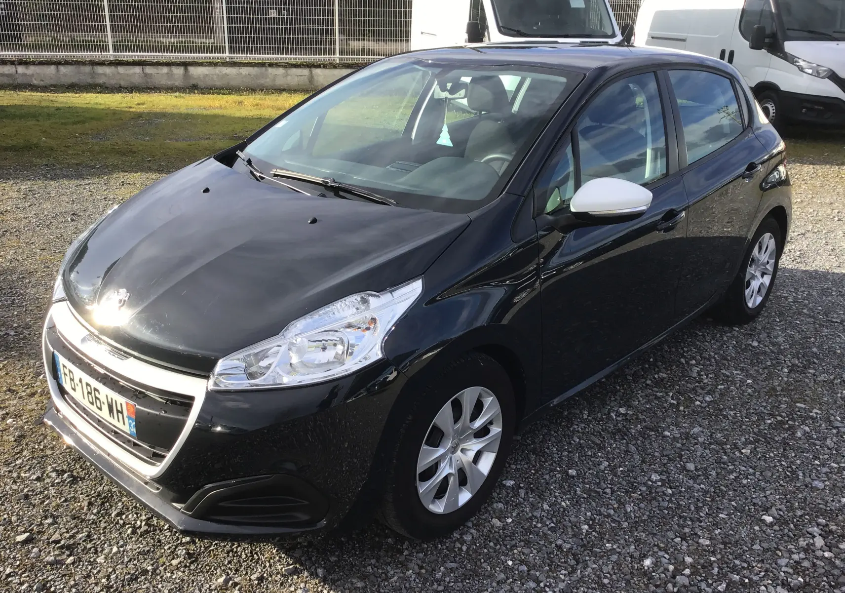 Peugeot 208 noire vue en 3/4 avant droit, avec rétroviseur blanc et jantes alliage argentées.