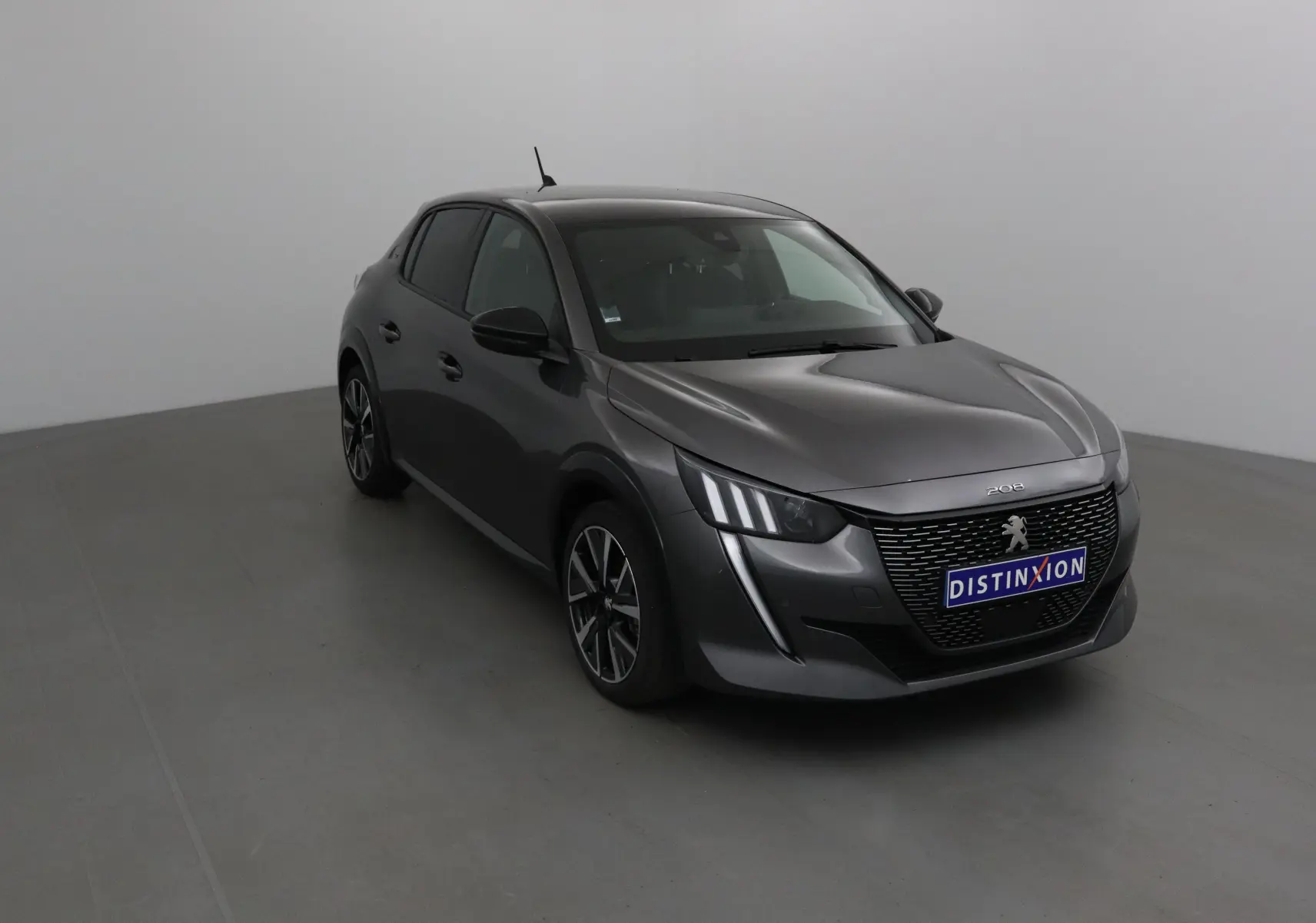 Peugeot 208 gris platinium/noir vue 3/4 avant droit dans un studio lumineux avec calandre distinctive.