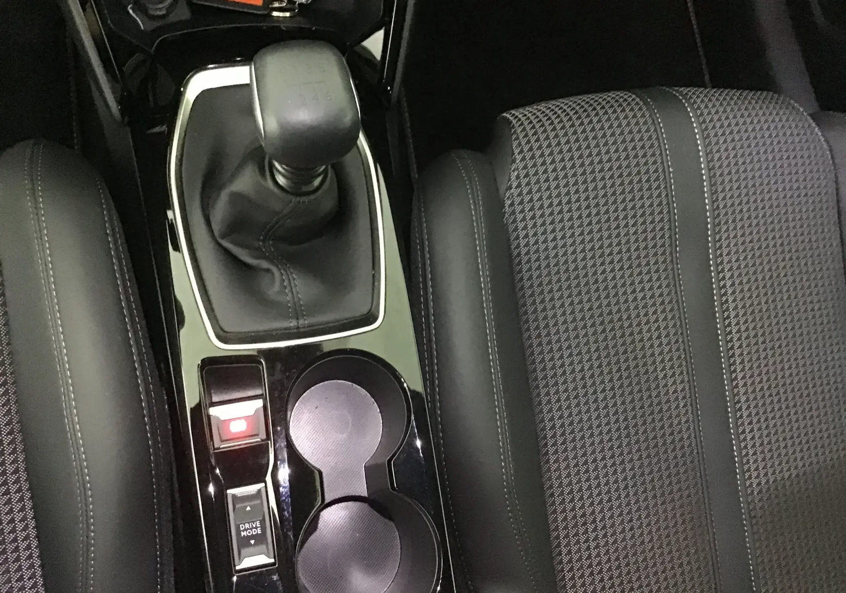 Vue rapprochée de la console centrale de la Peugeot 208 GT 2023 avec levier de vitesse manuel et sièges gris à motifs.