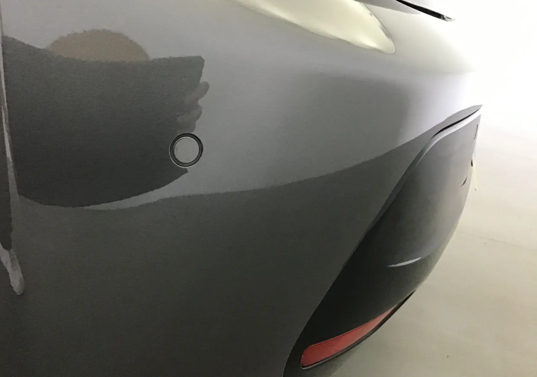 Gros plan sur le pare-chocs arrière gris platinium de la Peugeot 208 1.2 PureTech 100 GT avec capteur de recul visible.