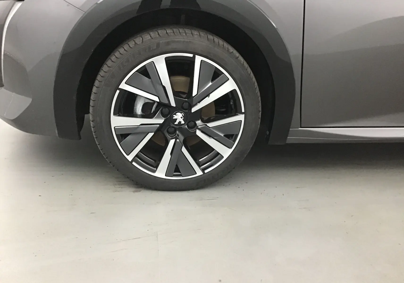 Gros plan sur la roue avant gauche de la Peugeot 208 1.2 PureTech 100 GT S&S gris platinium avec jante alliage noire et argent.