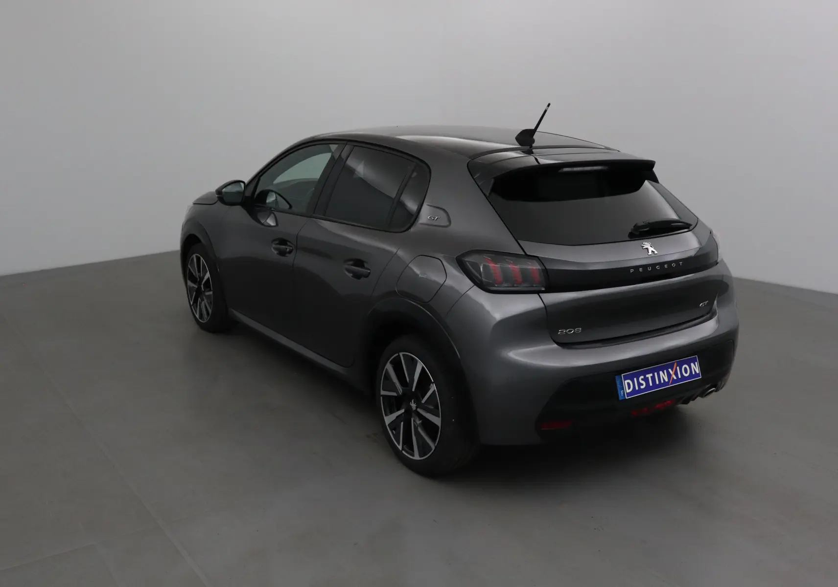 Peugeot 208 1.2 PureTech 100 GT gris platinium vue 3/4 arrière côté gauche en intérieur neutre.