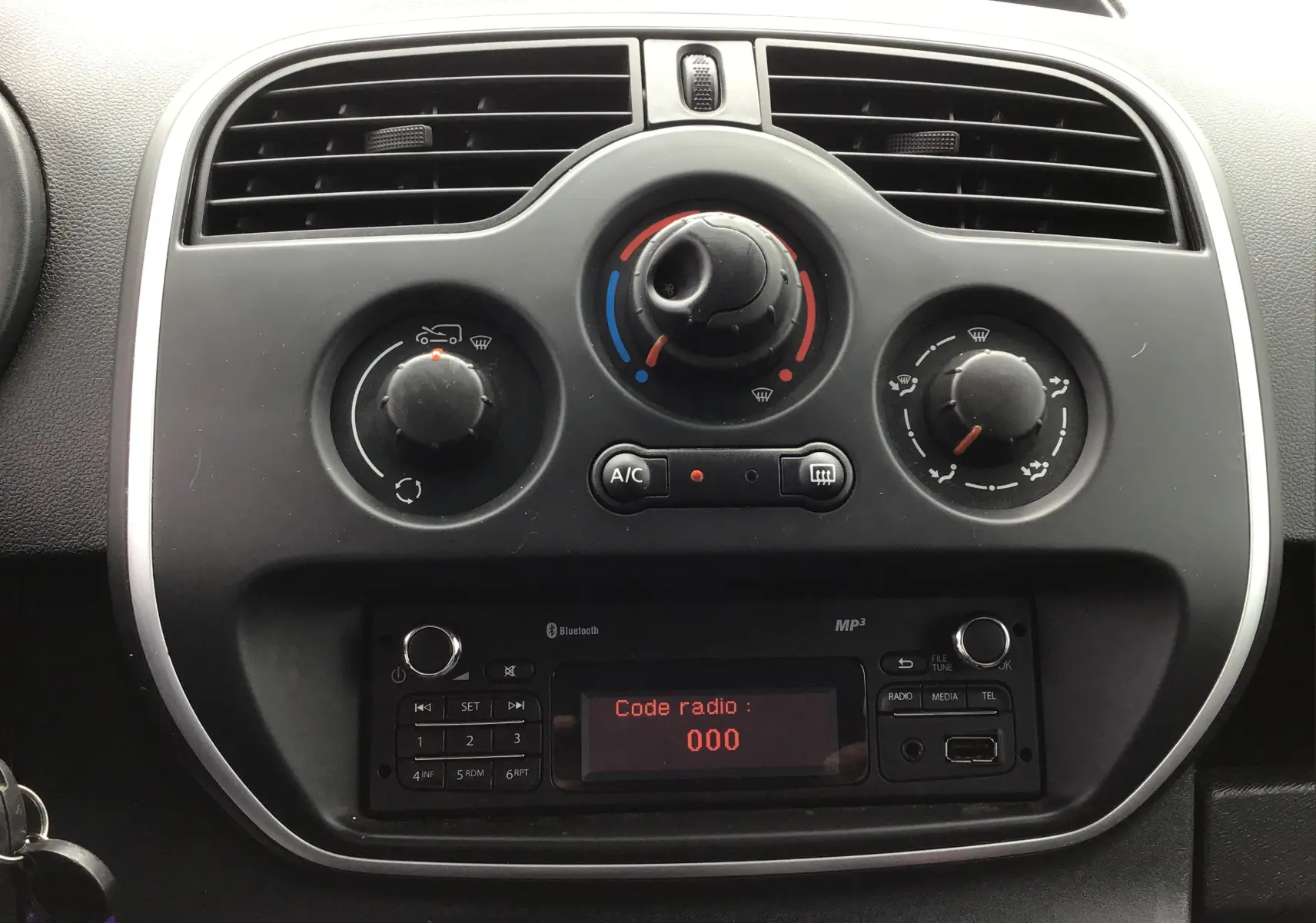 Tableau de bord du Renault Kangoo blanc 2019, vue frontale sur les commandes de climatisation et radio affichant "Code radio : 000".