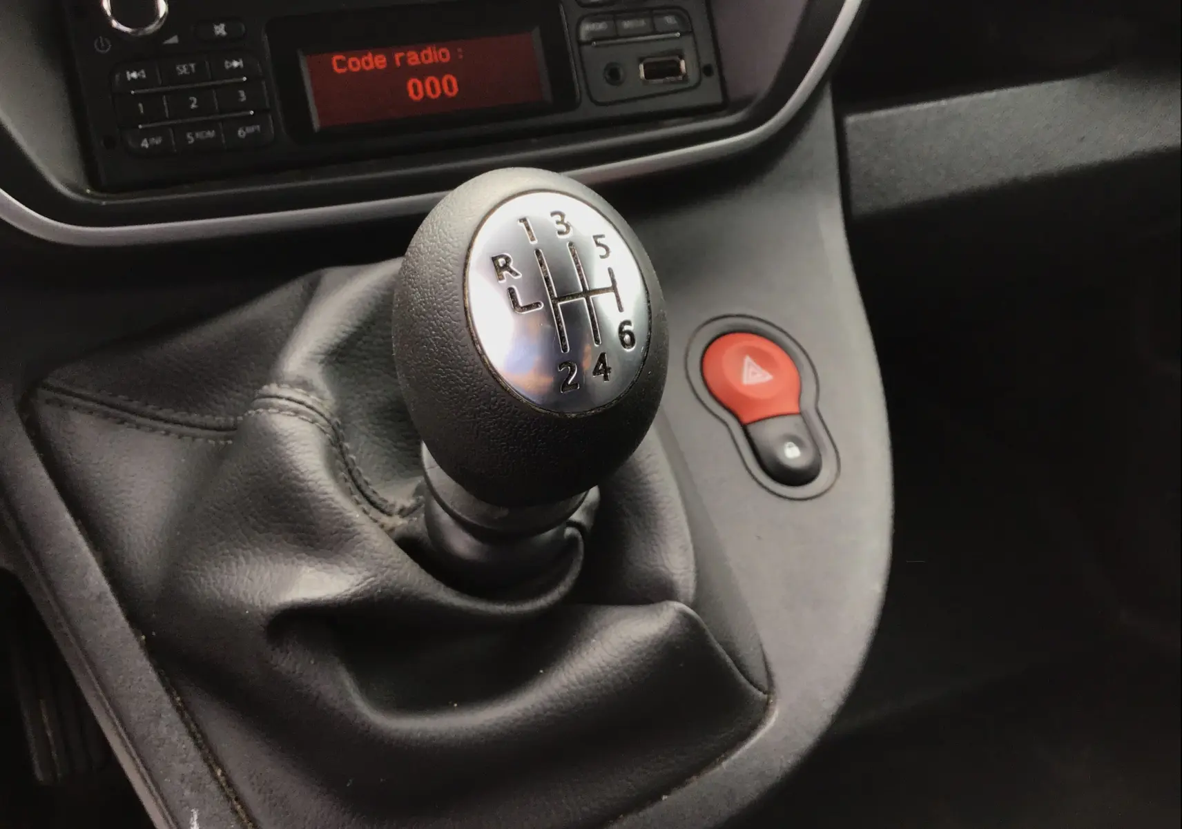 Gros plan sur le levier de vitesses manuel noir du Renault Kangoo blanc 2019, avec tableau de bord et bouton de warning rouge visible.