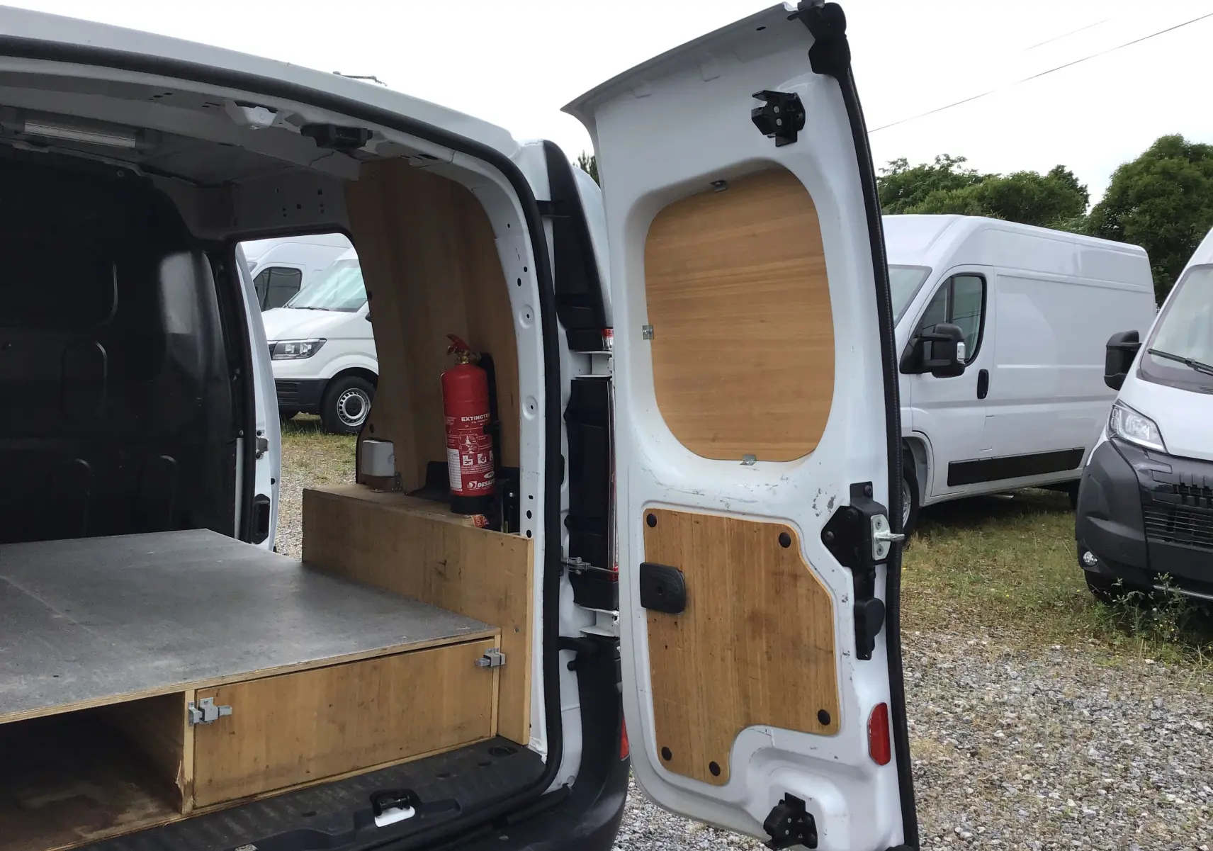 Vue arrière ouverte d'un Renault Kangoo blanc 2019 avec aménagements en bois et extincteur visible à l'intérieur.