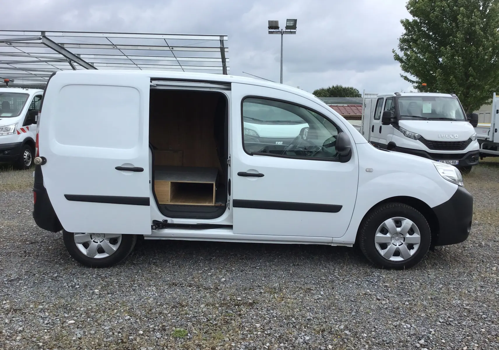Profil côté droit d'un Renault Kangoo blanc 2019 avec porte coulissante ouverte révélant un aménagement intérieur en bois.