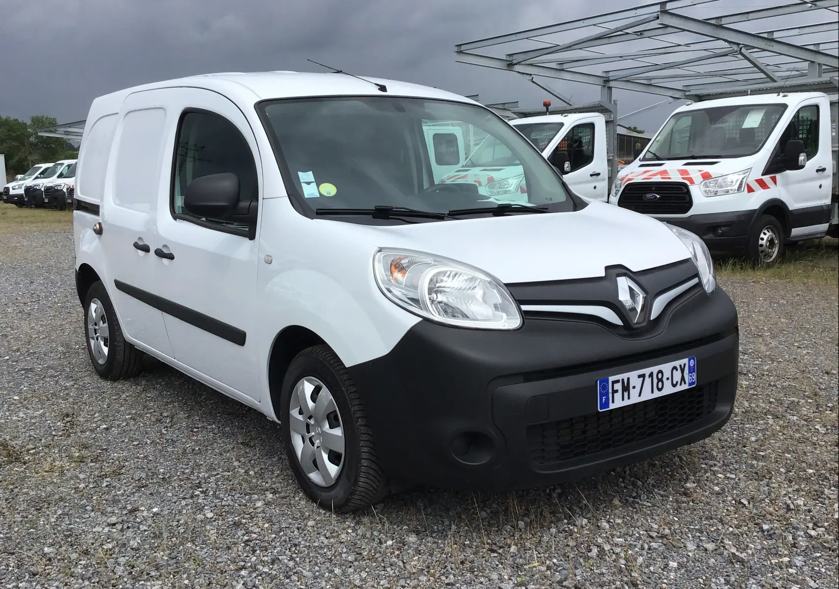 Renault Kangoo blanc vue 3/4 avant droit, fourgonnette utilitaire avec pare-chocs noirs et plaques françaises.