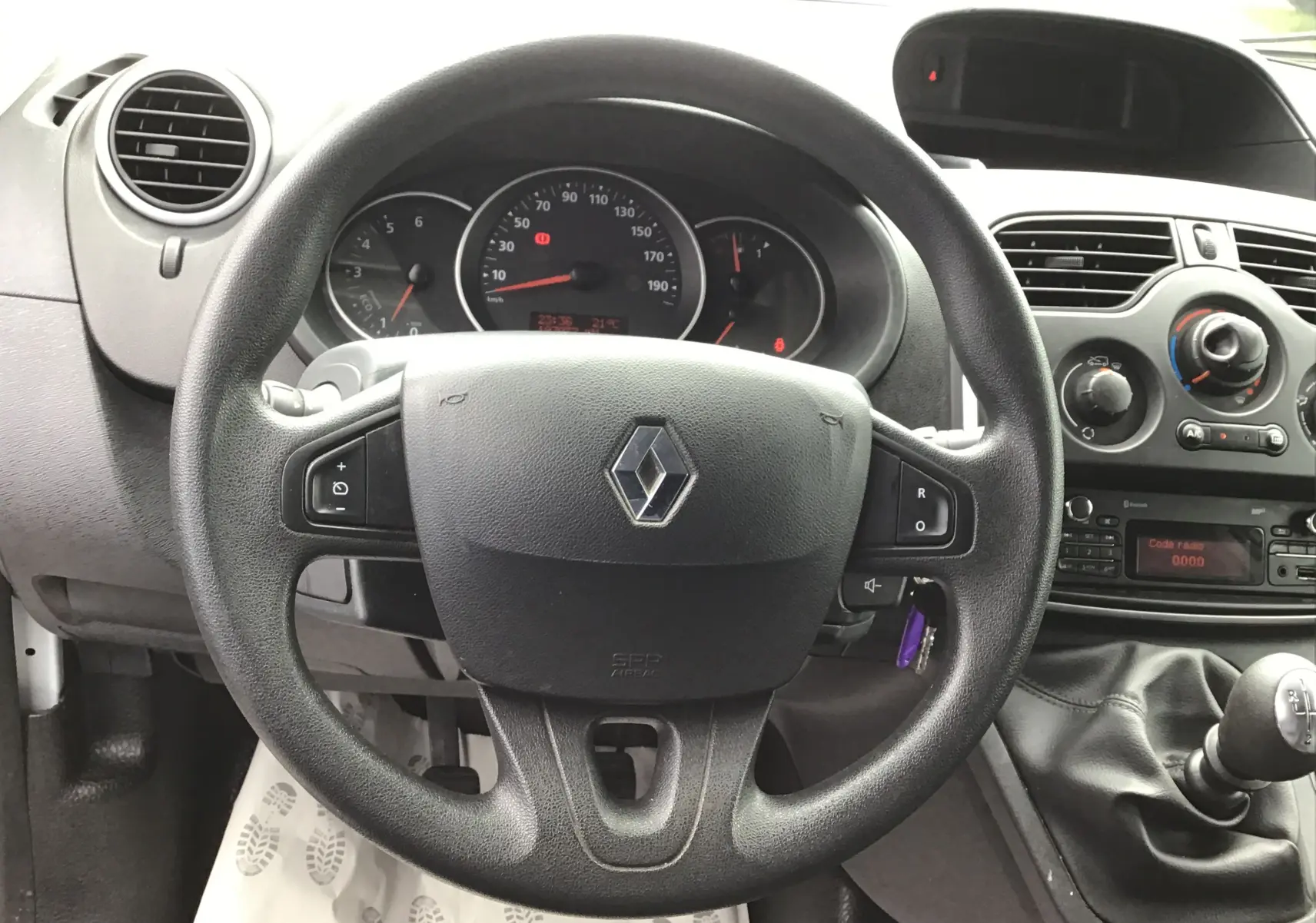 Vue intérieure centrée sur le volant noir Renault avec tableau de bord et console centrale d'un Kangoo blanc 2019.