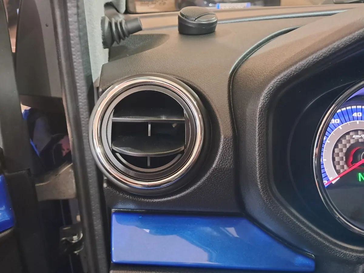 Détail de la ventilation côté gauche du tableau de bord bleu d'une Aixam Ambition 2026 avec compteur partiel visible.