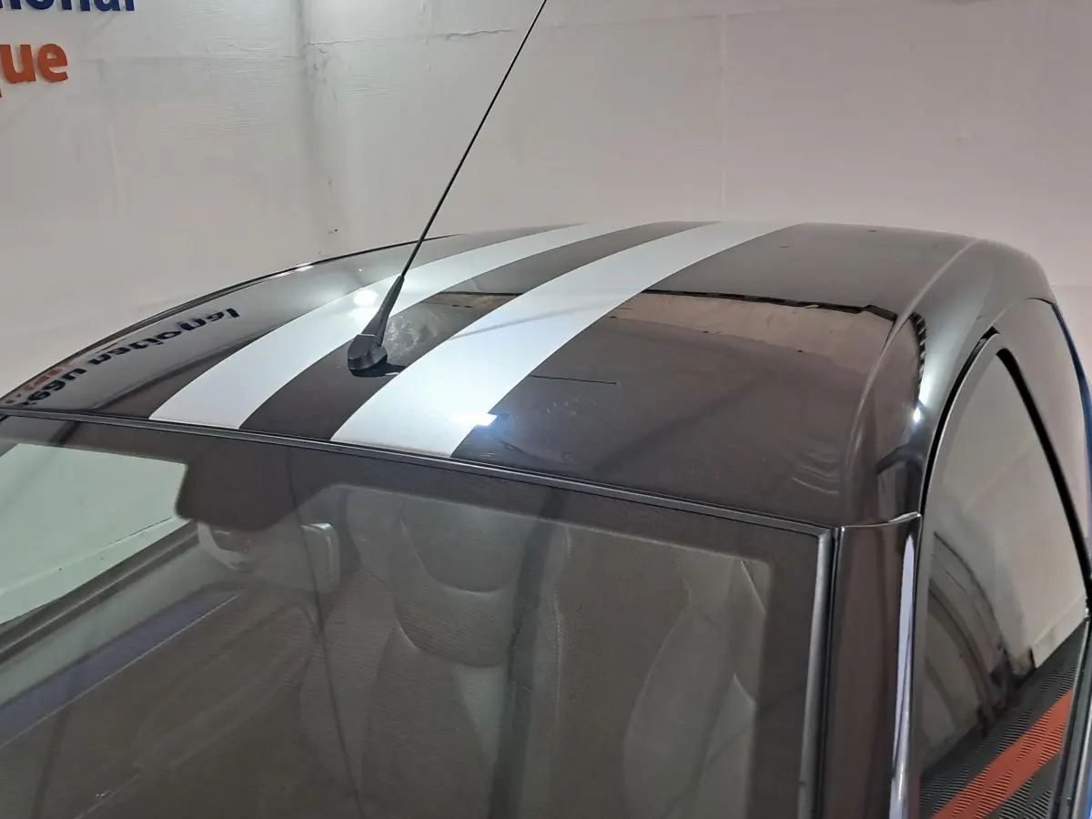 Vue plongeante sur le toit noir à bandes blanches d'une Aixam Ambition bleu, avec antenne centrale visible.