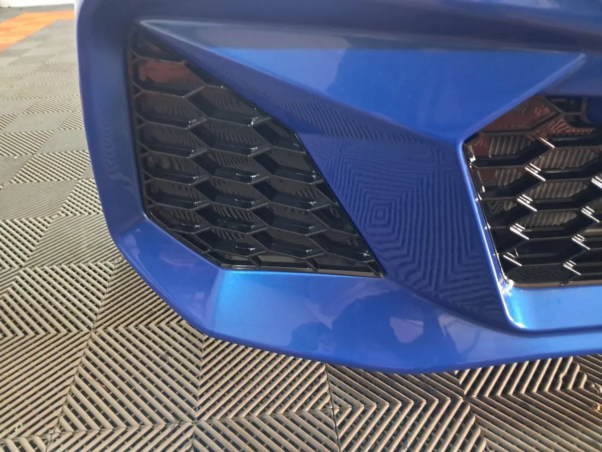 Gros plan sur la calandre avant droite bleu métallisé de l'AIXAM AMBITION 0.5 CITY GTO avec motif nid d'abeille noir.