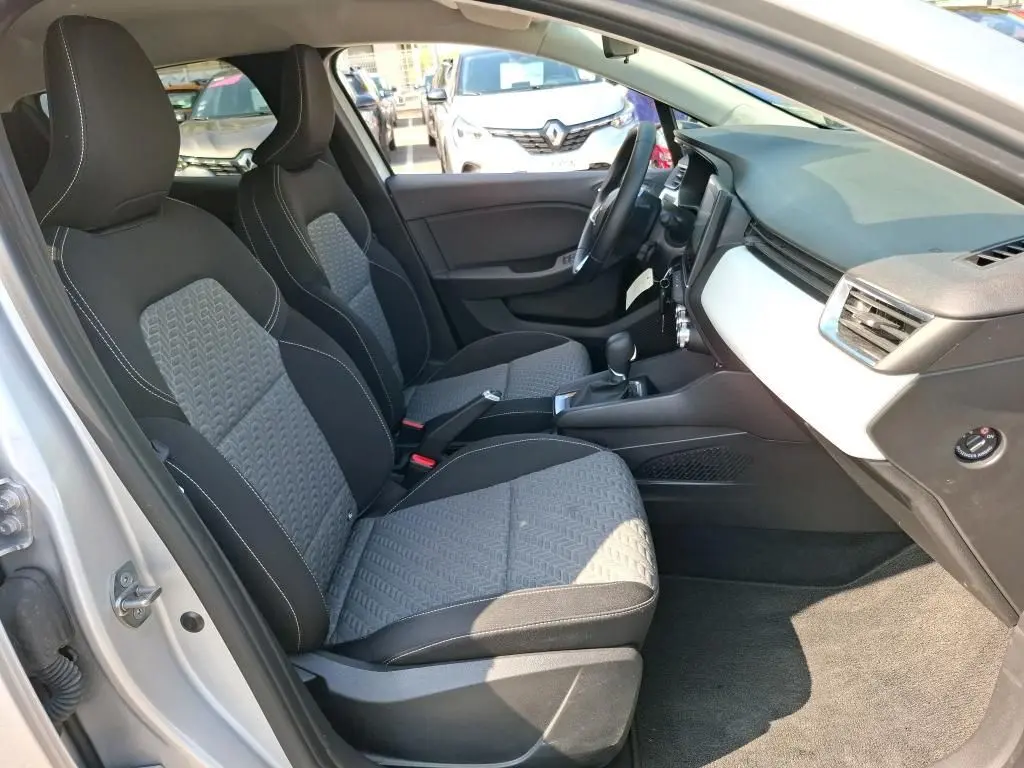 Vue intérieure côté conducteur de la Renault Clio gris platine 2023, sièges tissu bicolore et tableau de bord épuré.