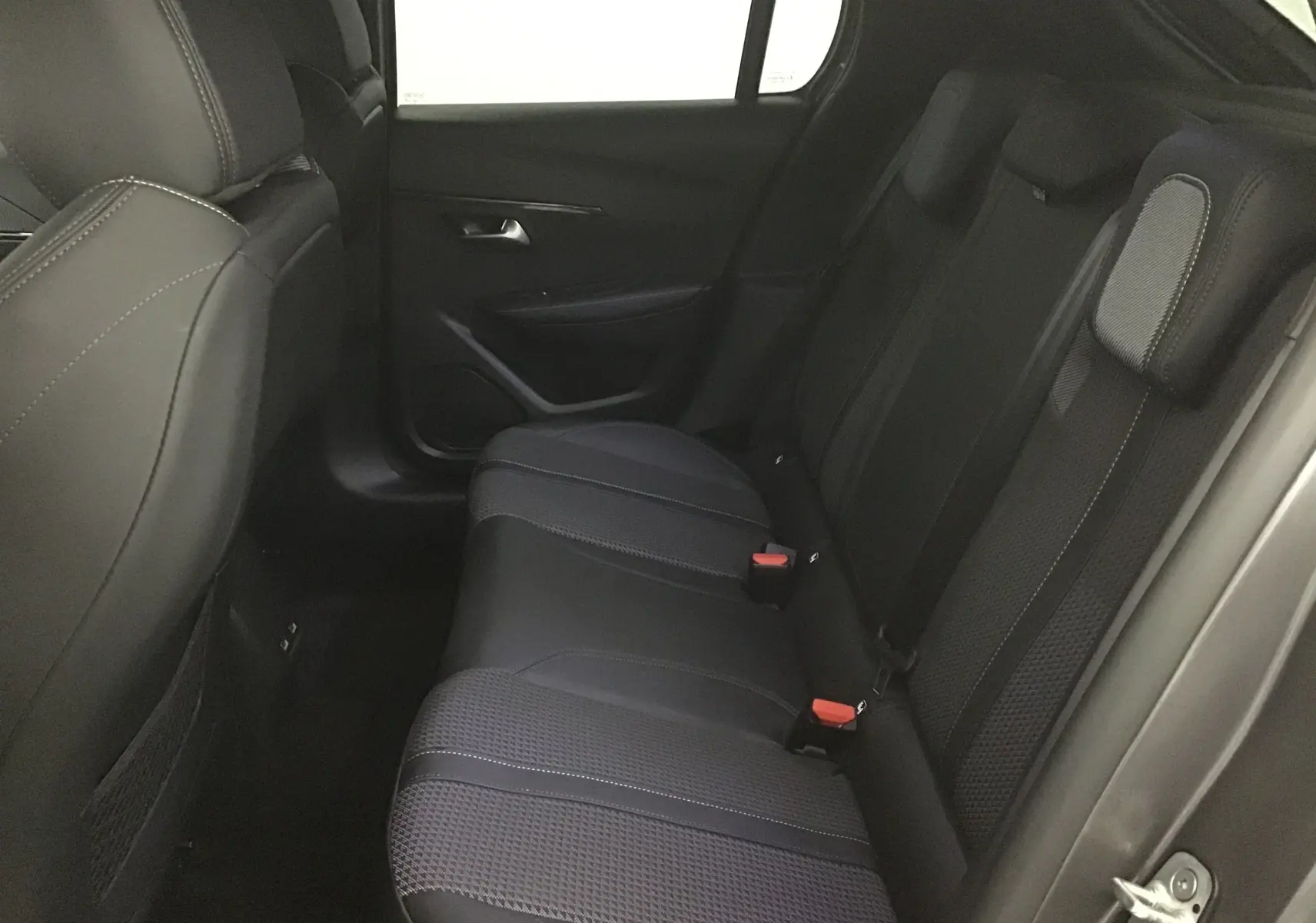 Vue intérieure arrière côté droit montrant les sièges arrière en tissu noir avec surpiqûres grises du Peugeot 208 2023.