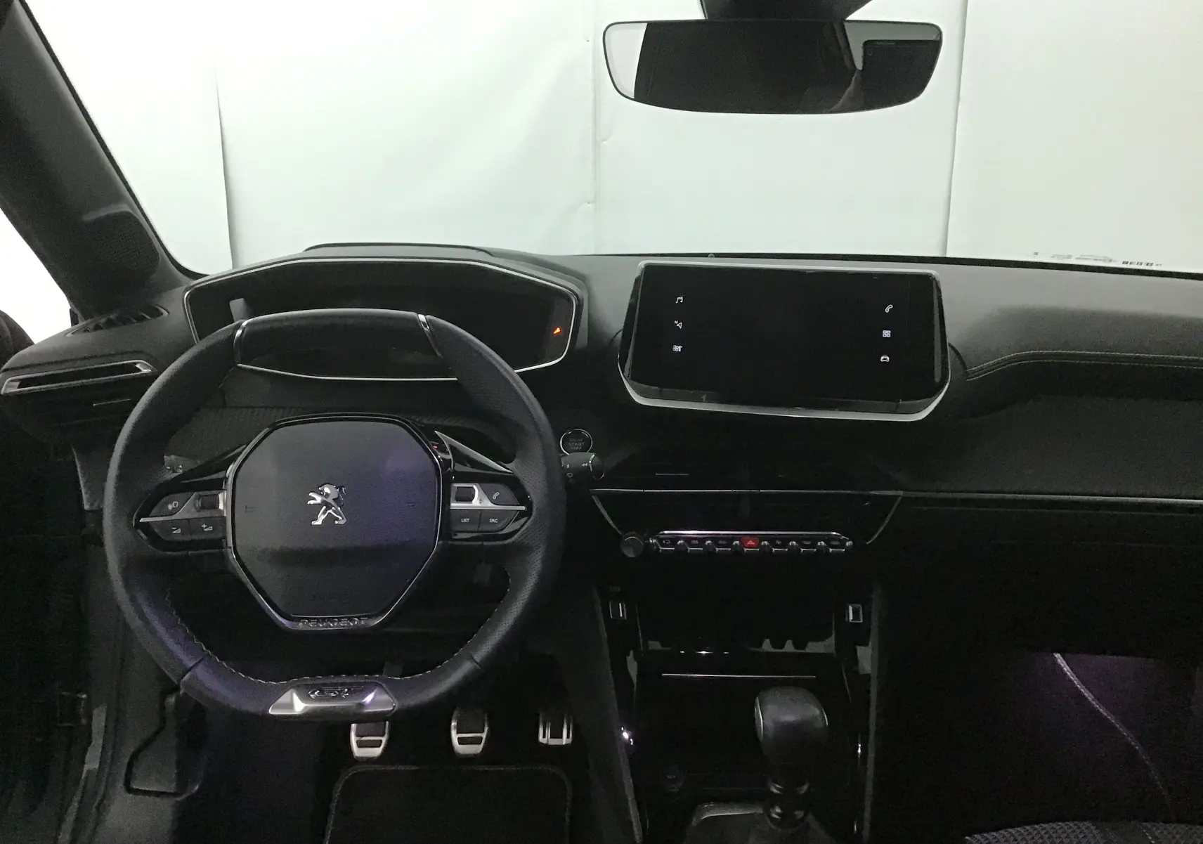 Vue intérieure frontale du tableau de bord noir de la Peugeot 208 1.2 PureTech 100 GT avec volant compact et écran tactile central.