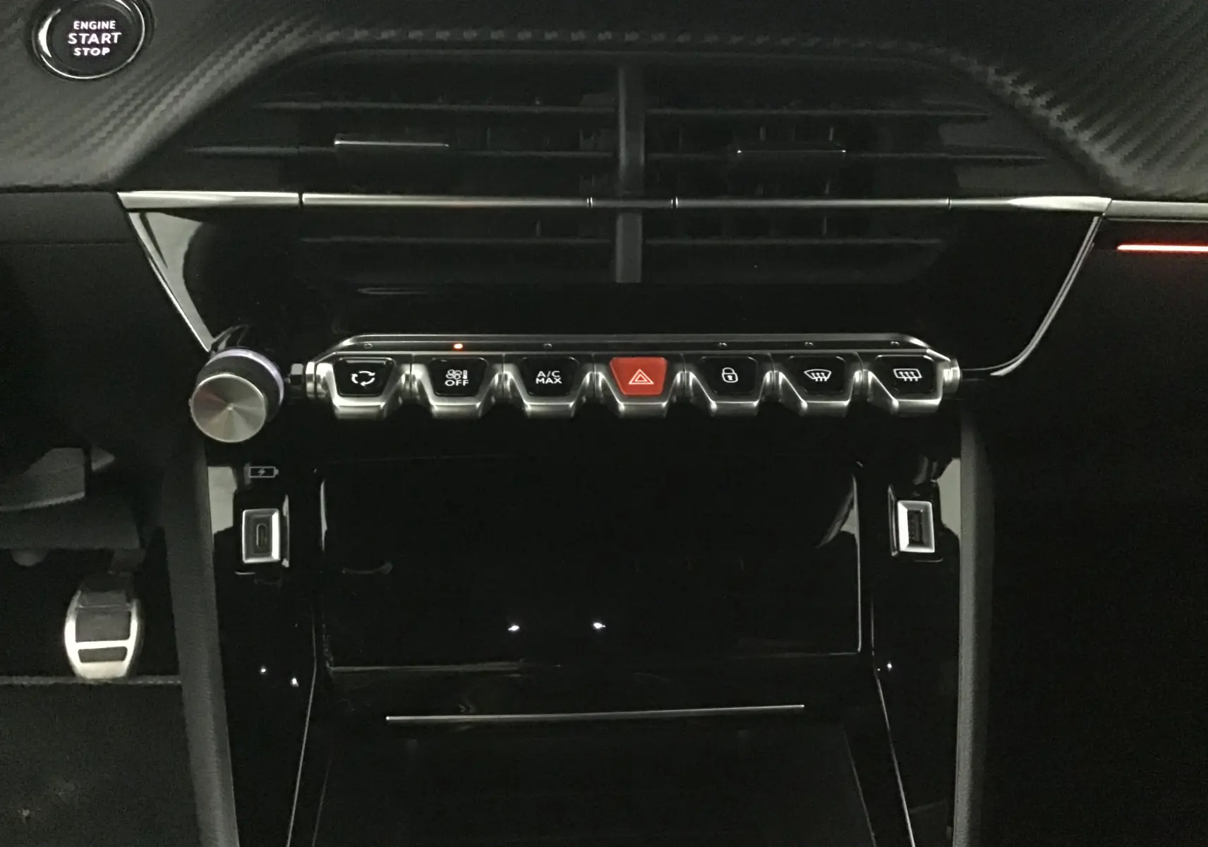 Tableau de bord intérieur de Peugeot 208 2023, vue frontale centrée sur les commandes et boutons chromés avec bouton d'alerte rouge.