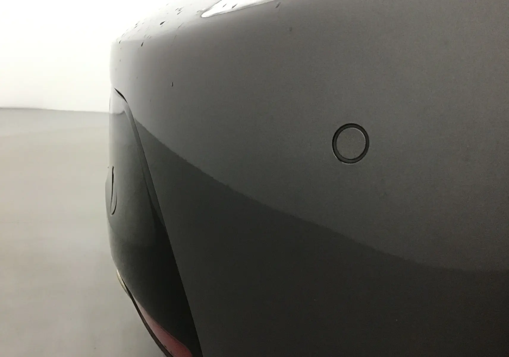 Gros plan sur le pare-chocs arrière gris platinium du Peugeot 208 1.2 PureTech 100 GT avec capteur de recul visible.