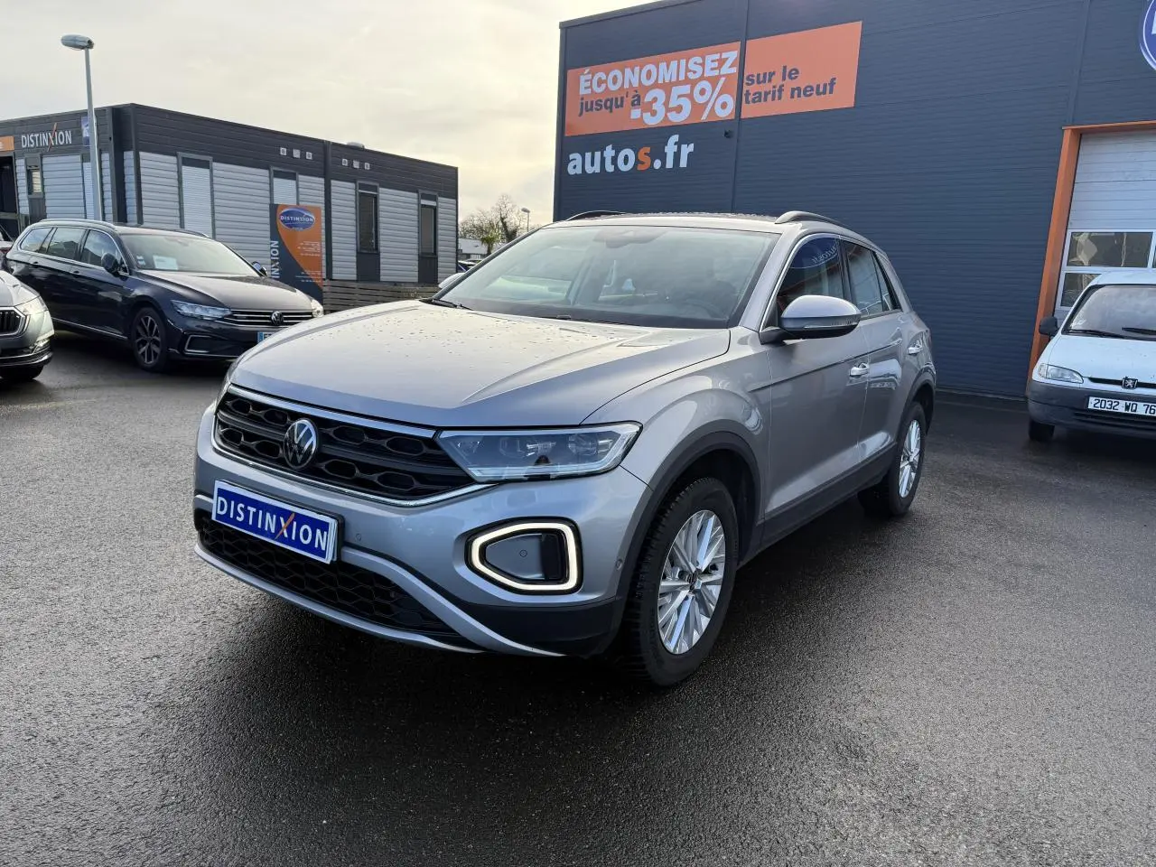 Volkswagen T-Roc gris pyrite vu en 3/4 avant droit sur parking devant un bâtiment commercial autos.fr