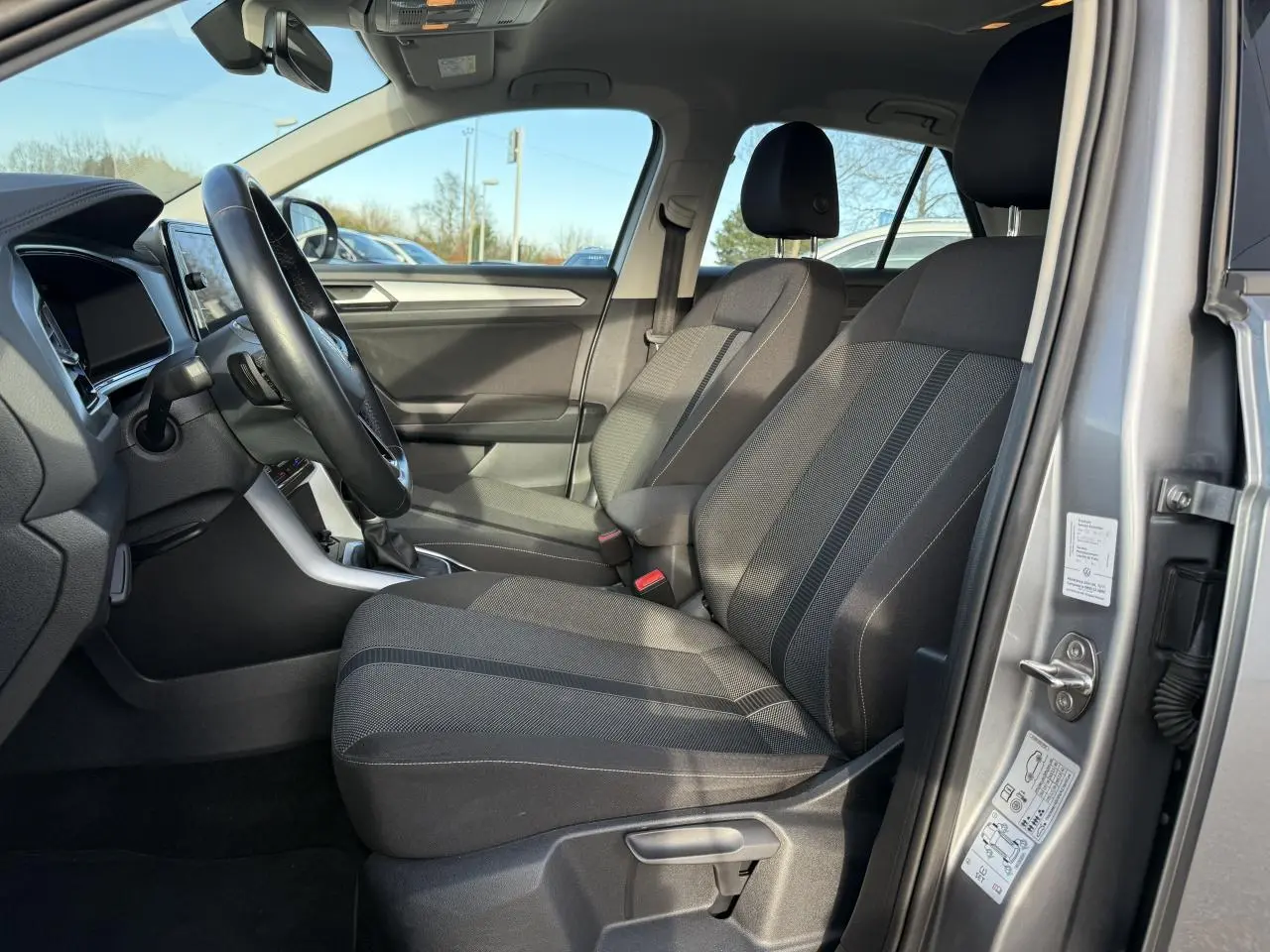 Vue intérieure côté conducteur du Volkswagen T-Roc gris pyrite 2022, montrant les sièges avant et le volant multifonction en cuir.