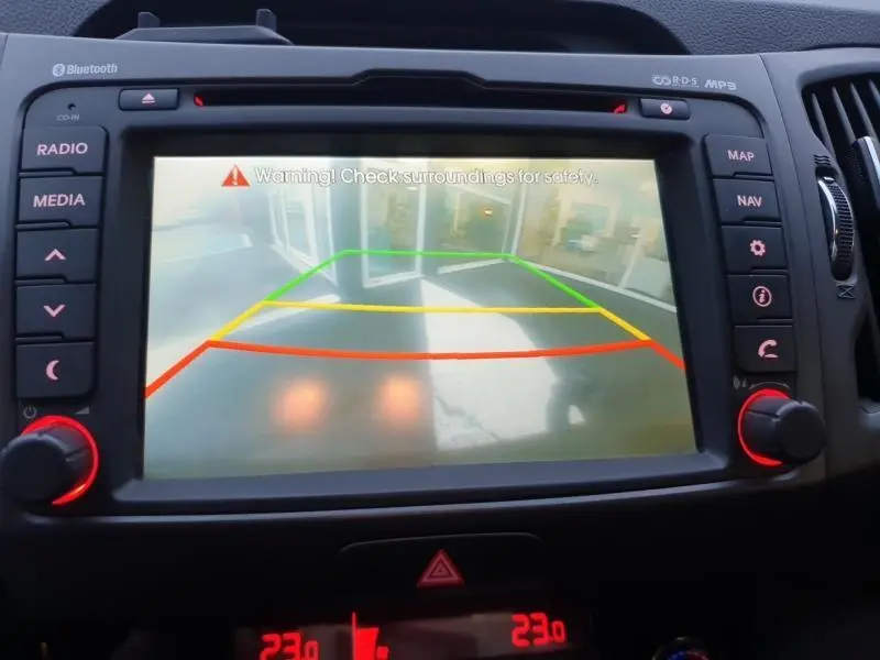 Écran de caméra de recul du Kia Sportage blanc 2013 montrant les lignes de guidage colorées sur un sol extérieur.