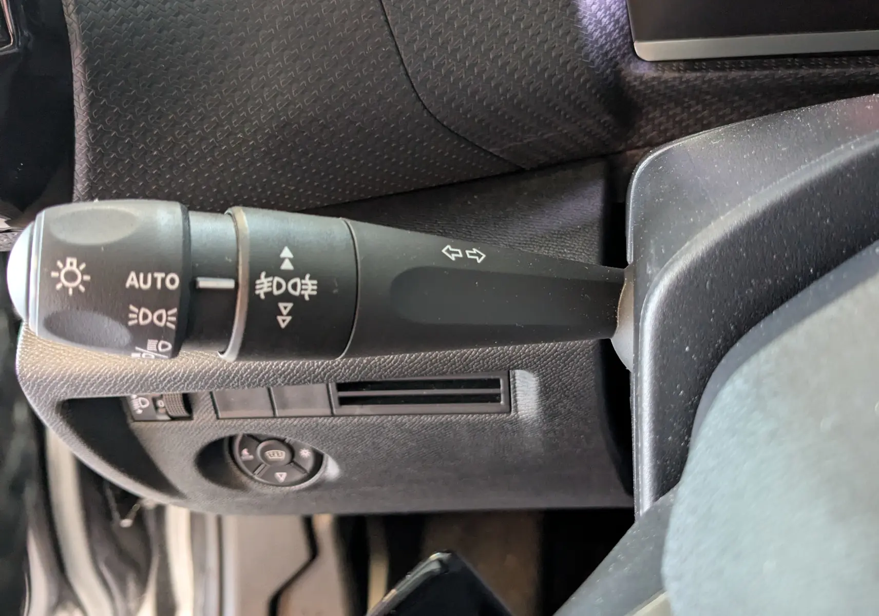 Gros plan sur la commande des feux et clignotants à gauche du volant dans l'habitacle gris noir d'une Citroën C4 2024.