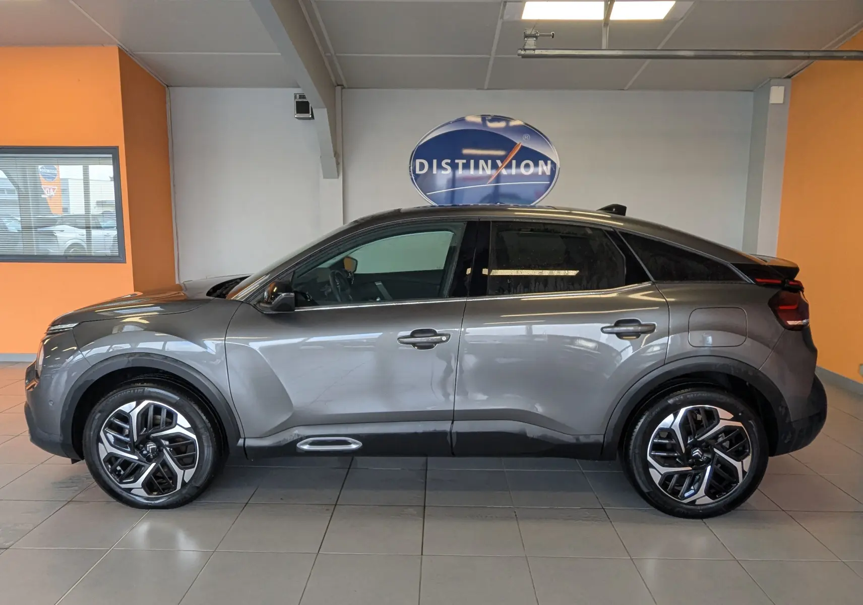 Profil côté gauche d'une Citroën C4 gris platinium 2024 avec jantes alliage 18 pouces et toit panoramique en intérieur showroom.