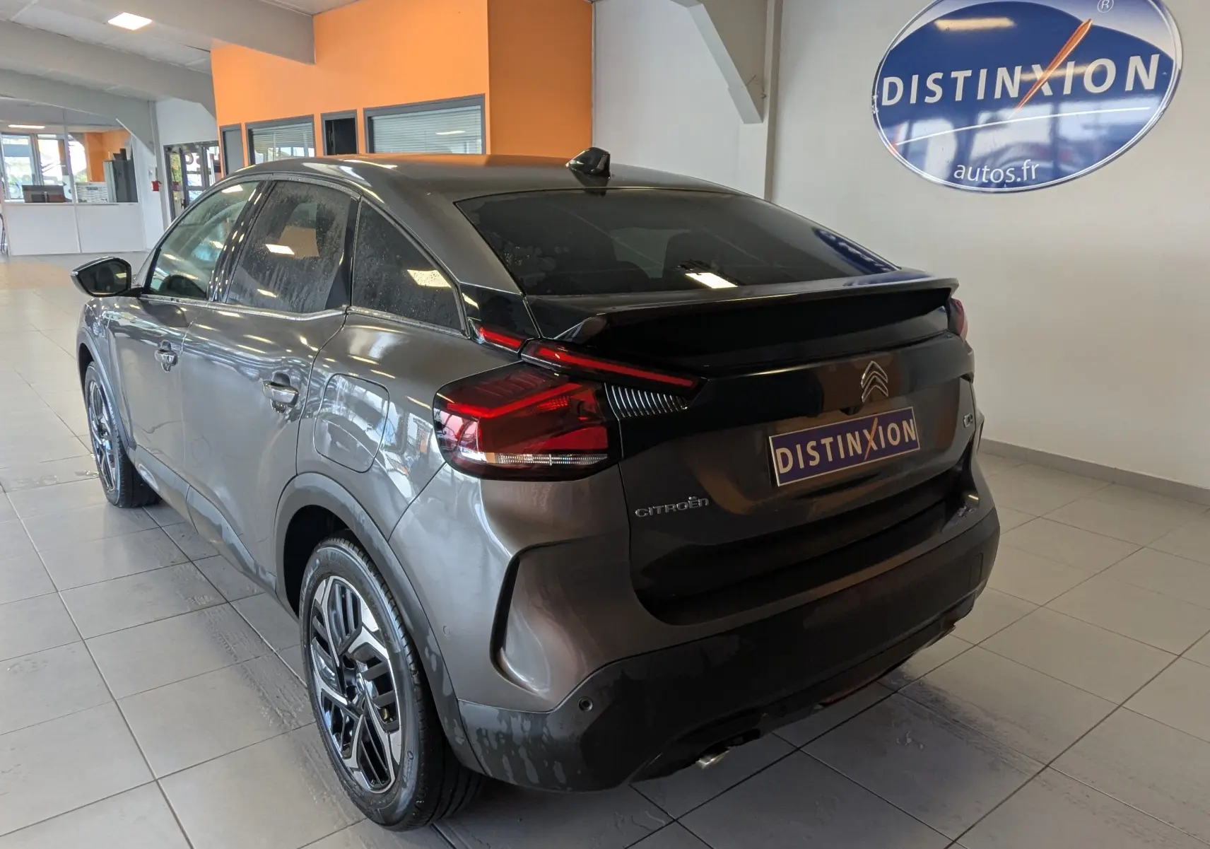 Vue 3/4 arrière droite d'une Citroën C4 gris platinium avec toit panoramique et jantes alliage 18 pouces en showroom.