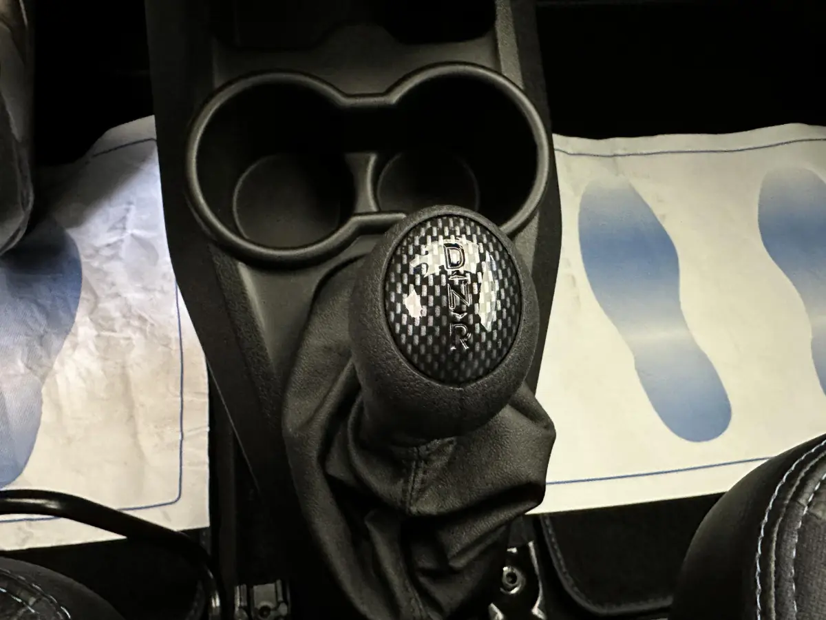 Gros plan sur le levier de vitesses automatique noir avec marquage D, N, R, T dans l'habitacle d'une Aixam rouge.