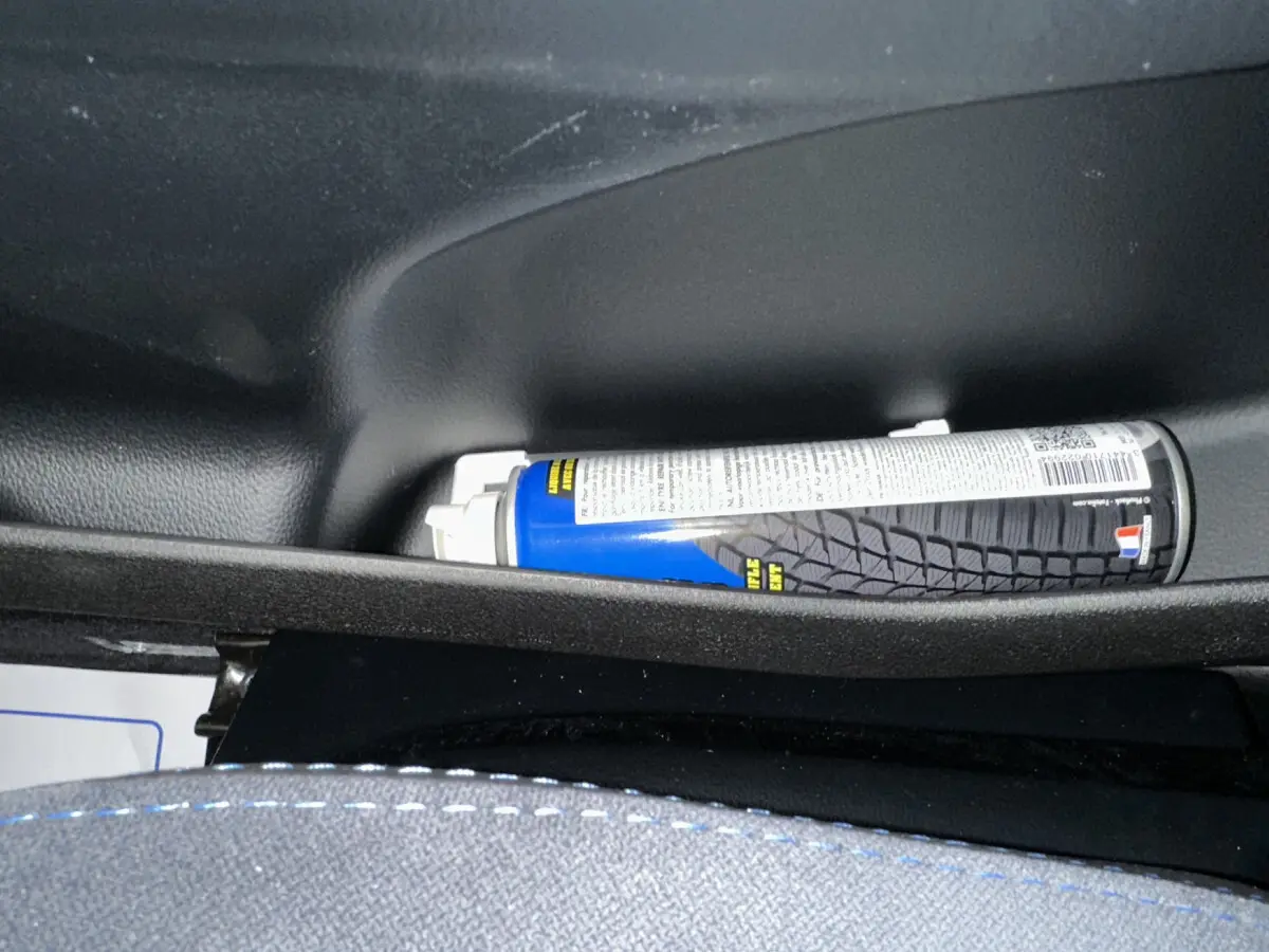 Vue rapprochée de l'intérieur d'une Aixam Ambition rouge 2026, montrant un rangement avec un spray et une couture bleue sur le siège.