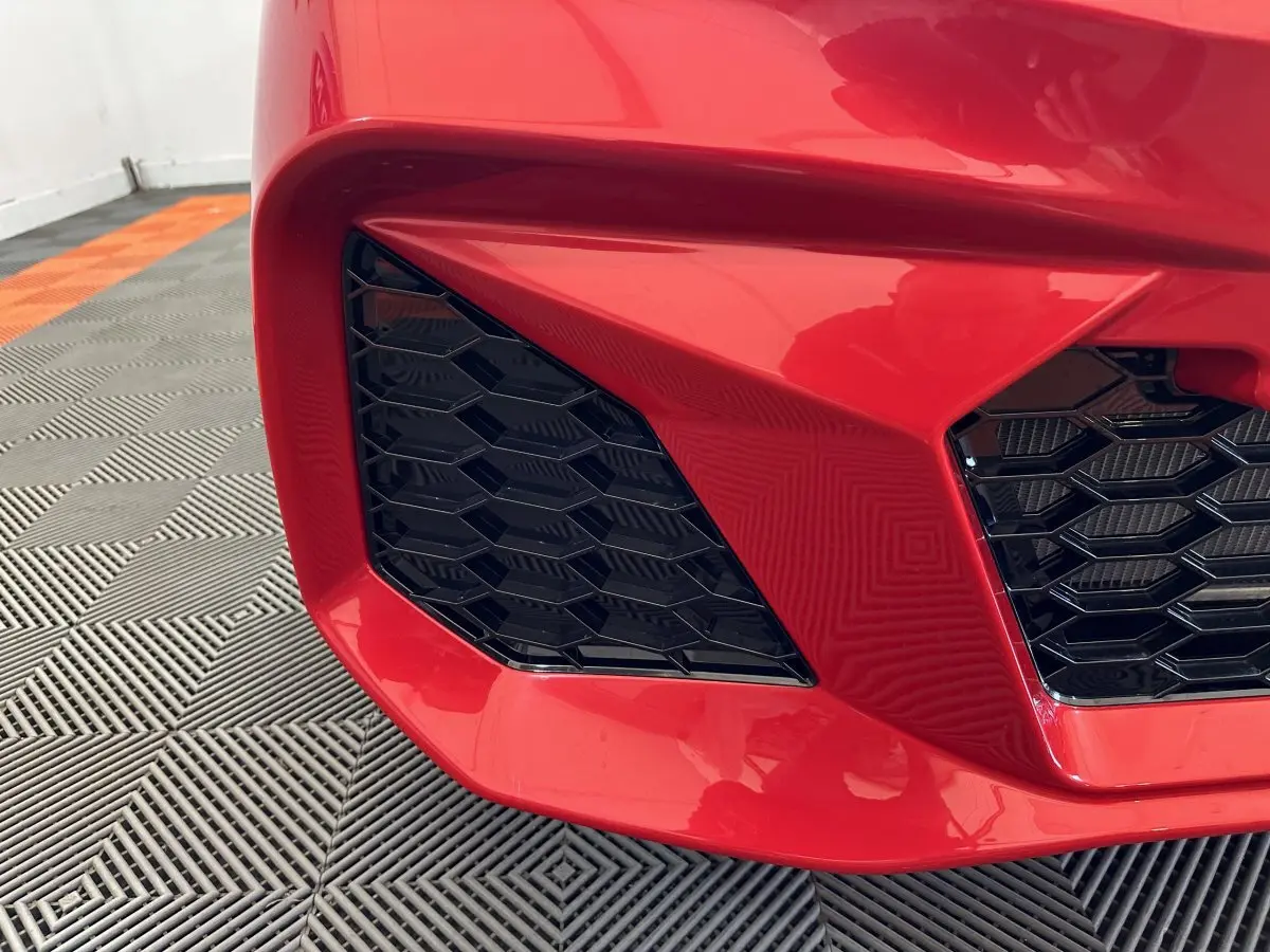 Gros plan sur la calandre avant gauche rouge de l'AIXAM AMBITION 0.5 CITY COUPE GTI E5+ avec grille noire hexagonale.