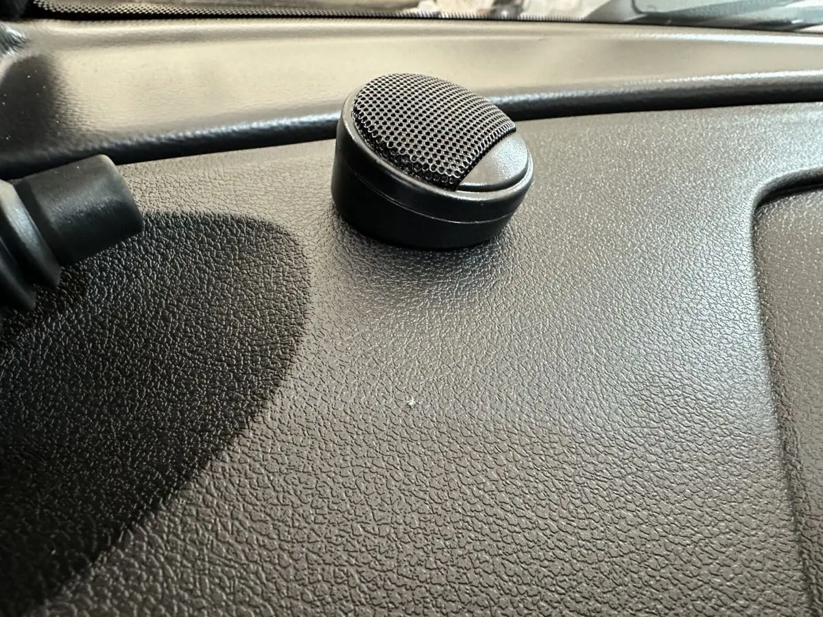 Gros plan sur un haut-parleur noir posé sur le tableau de bord texturé d'une Aixam Ambition rouge.