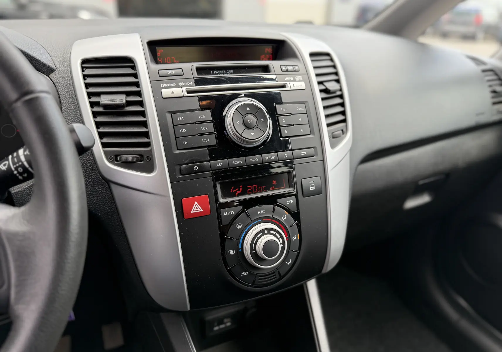 Vue intérieure centrée sur la console centrale noire et grise du Kia Venga 1.4 i 90 ACTIVE avec commandes climatisation et audio.