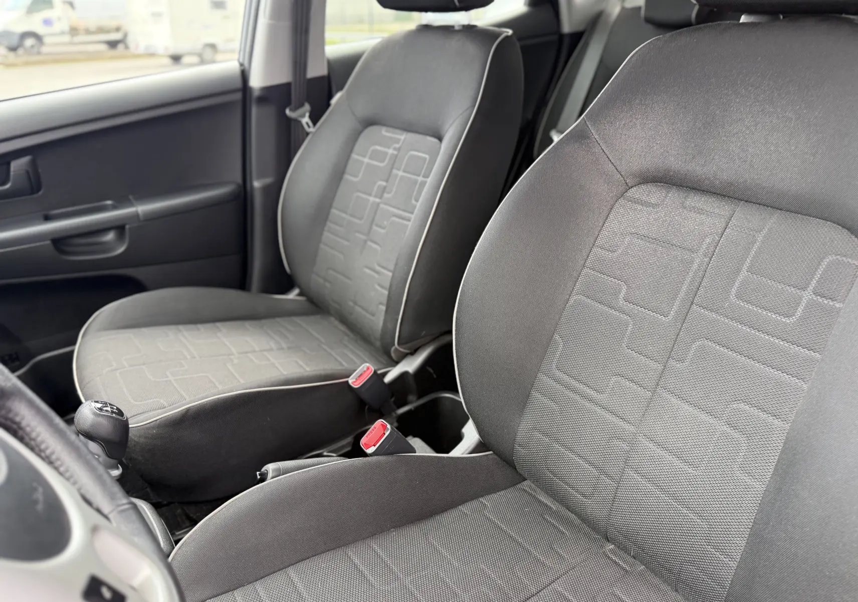 Vue intérieure rapprochée des sièges avant en tissu gris d'une KIA VENGA 1.4 i 90 ACTIVE de 2013 avec boîte manuelle.