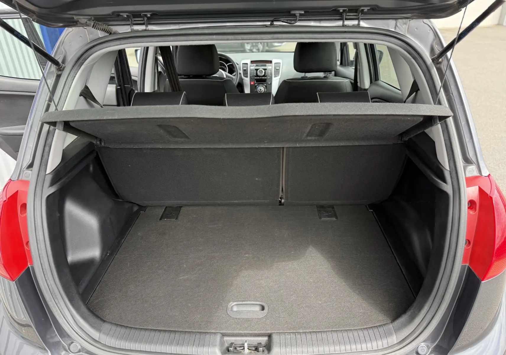 Coffre ouvert d'une KIA VENGA gris vue arrière, montrant l'espace de chargement et l'intérieur des sièges arrière.
