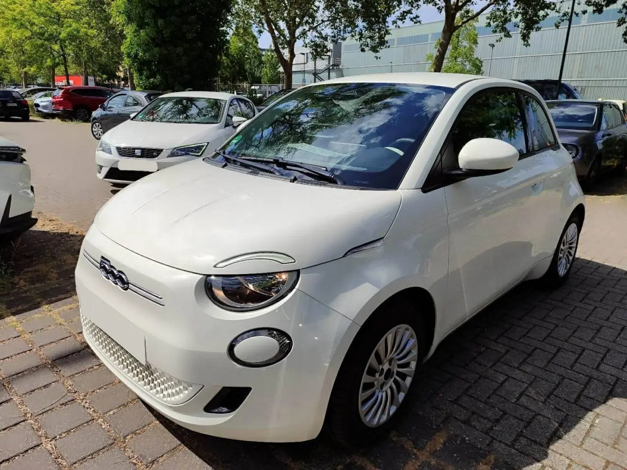 Vue 3/4 avant droite d'une Fiat 500 électrique blanche, avec logo distinctif et jantes multibranches visibles.