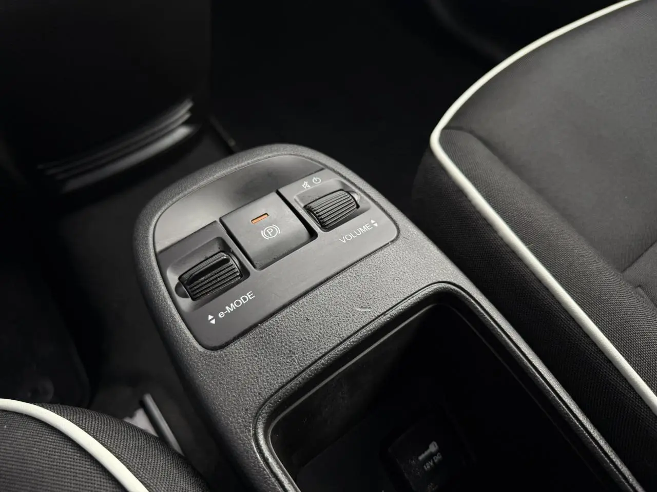 Gros plan sur la console centrale de la Fiat 500 électrique blanche, montrant les commandes e-mode et volume entre les sièges noirs avec surpiqûres blanches.