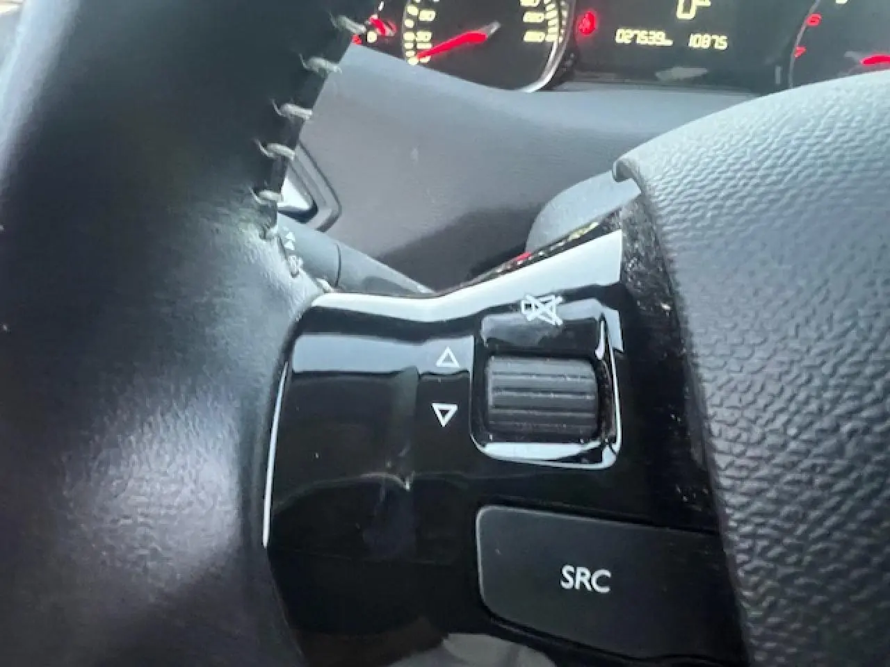 Gros plan sur les commandes audio au volant noir de la Peugeot 308 blanche, avec tableau de bord en arrière-plan.