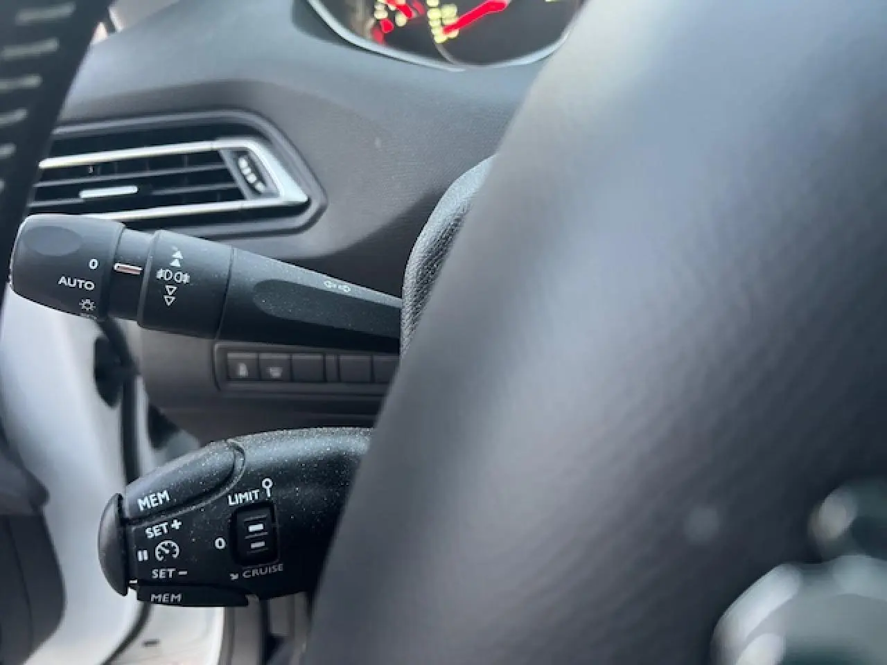 Gros plan sur les commandes au volant côté gauche d'une Peugeot 308 blanche, mettant en valeur les fonctions régulateur et éclairage.