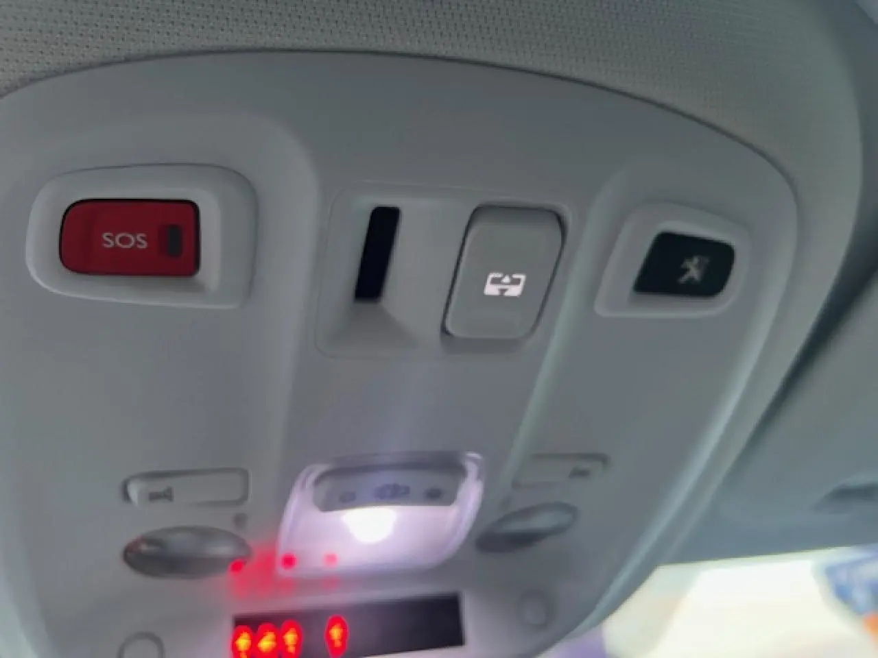 Vue en gros plan du panneau de commandes au plafond intérieur du Peugeot 308 blanc, avec bouton SOS rouge et éclairage blanc.