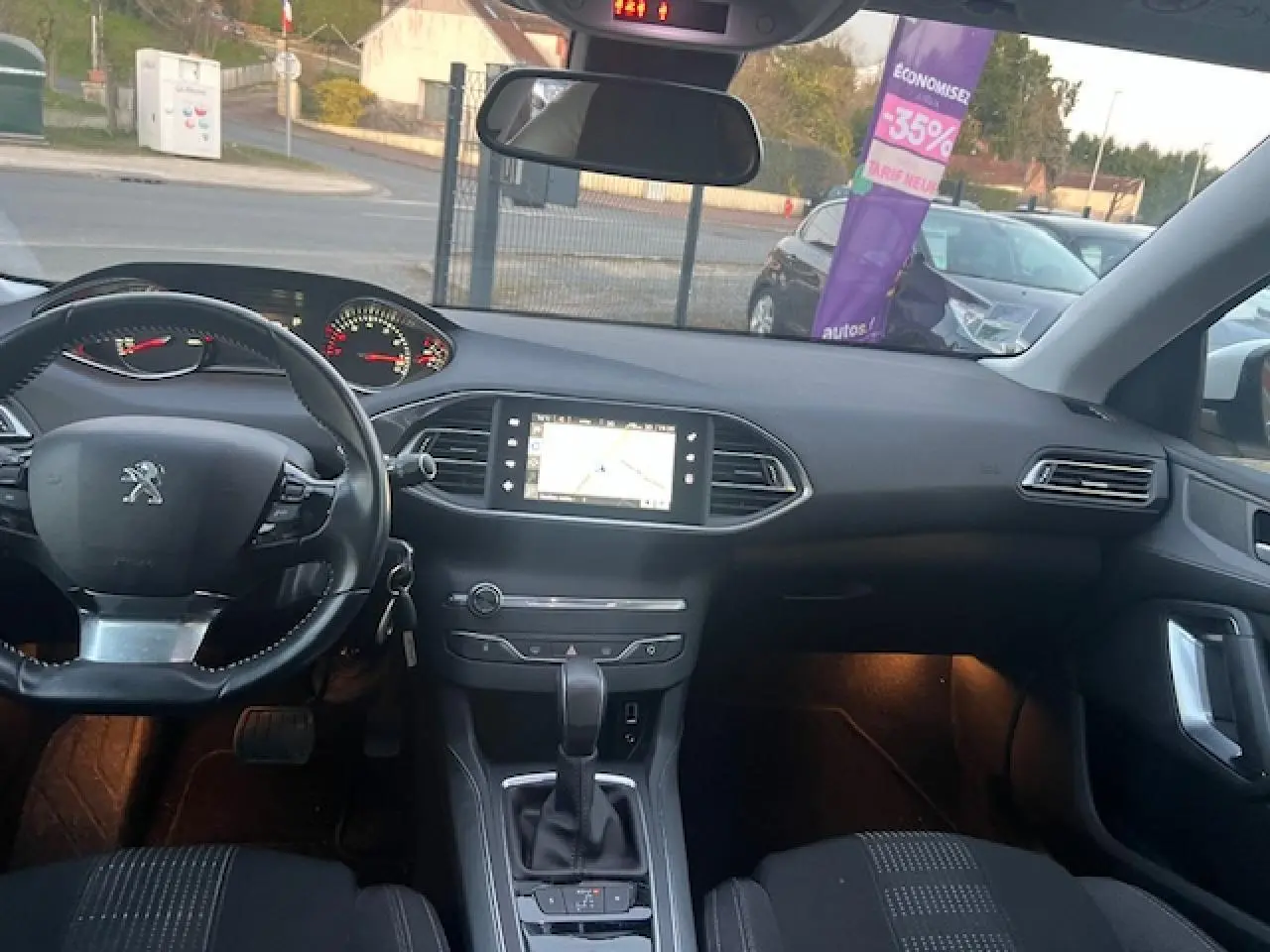 Intérieur de Peugeot 308 blanc 2017 vu de face, tableau de bord avec écran tactile de navigation allumé.