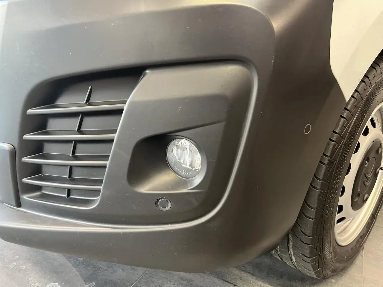 Gros plan sur le pare-chocs avant droit noir avec antibrouillard et roue acier du Citroën Jumpy blanc.
