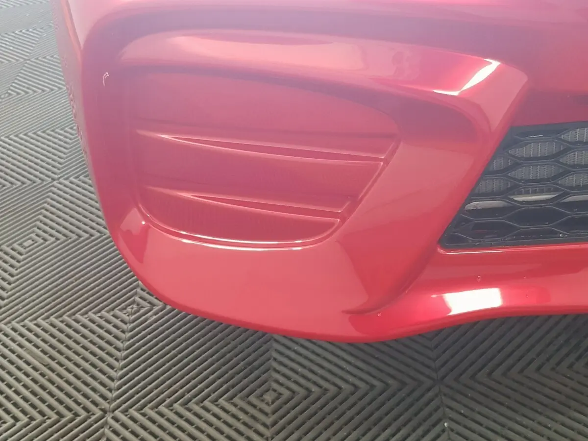 Gros plan sur le pare-chocs avant rouge de l'AIXAM AMBITION 0.5 CITY PACK avec grille noire visible à droite.